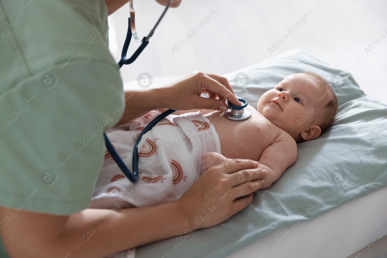 Pediatrician examining baby with stethoscope at table in clinic, closeup Photo of Pediatrician examining baby with stethoscope at table in clinic, closeup