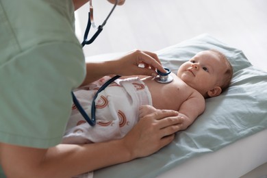 Photo of Pediatrician examining baby with stethoscope at table in clinic, closeup