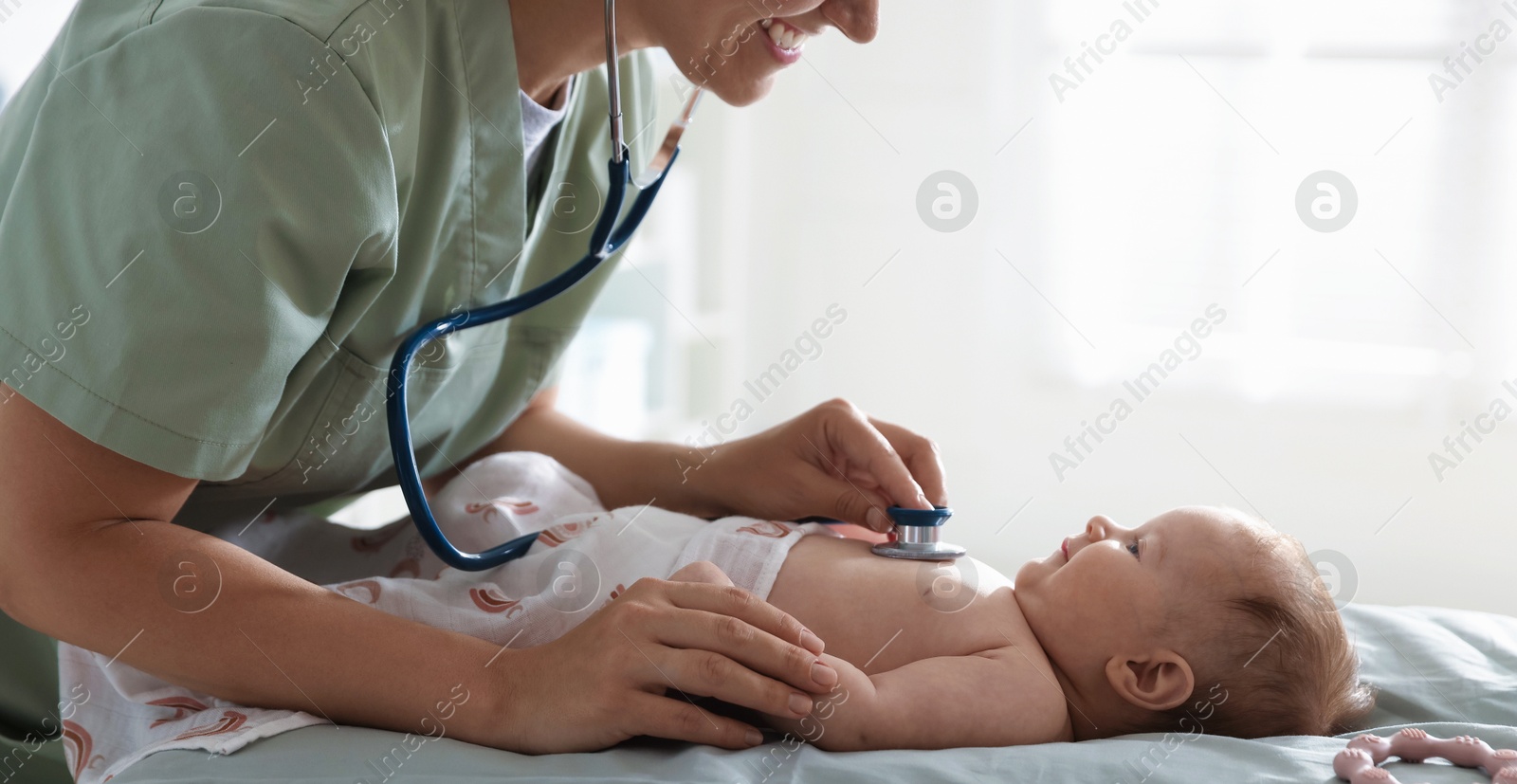Pediatrician examining baby with stethoscope at table in clinic, closeup Photo of Pediatrician examining baby with stethoscope at table in clinic, closeup