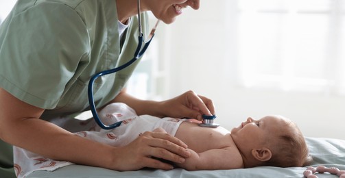 Photo of Pediatrician examining baby with stethoscope at table in clinic, closeup
