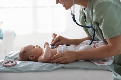 Photo of Pediatrician examining baby with stethoscope at table in clinic, closeup