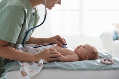 Photo of Pediatrician examining baby with stethoscope at table in clinic, closeup