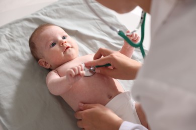 Photo of Pediatrician examining baby with stethoscope at table in clinic, closeup