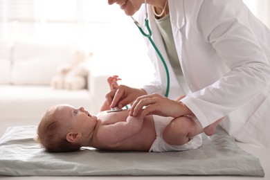 Photo of Pediatrician examining baby with stethoscope at table in clinic, closeup