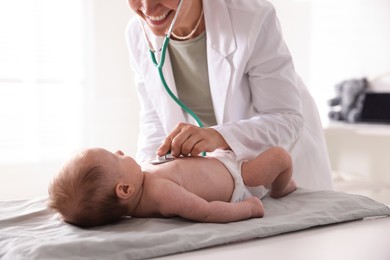 Photo of Pediatrician examining baby with stethoscope at table in clinic, closeup