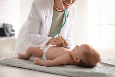 Photo of Pediatrician examining baby with stethoscope at table in clinic, closeup