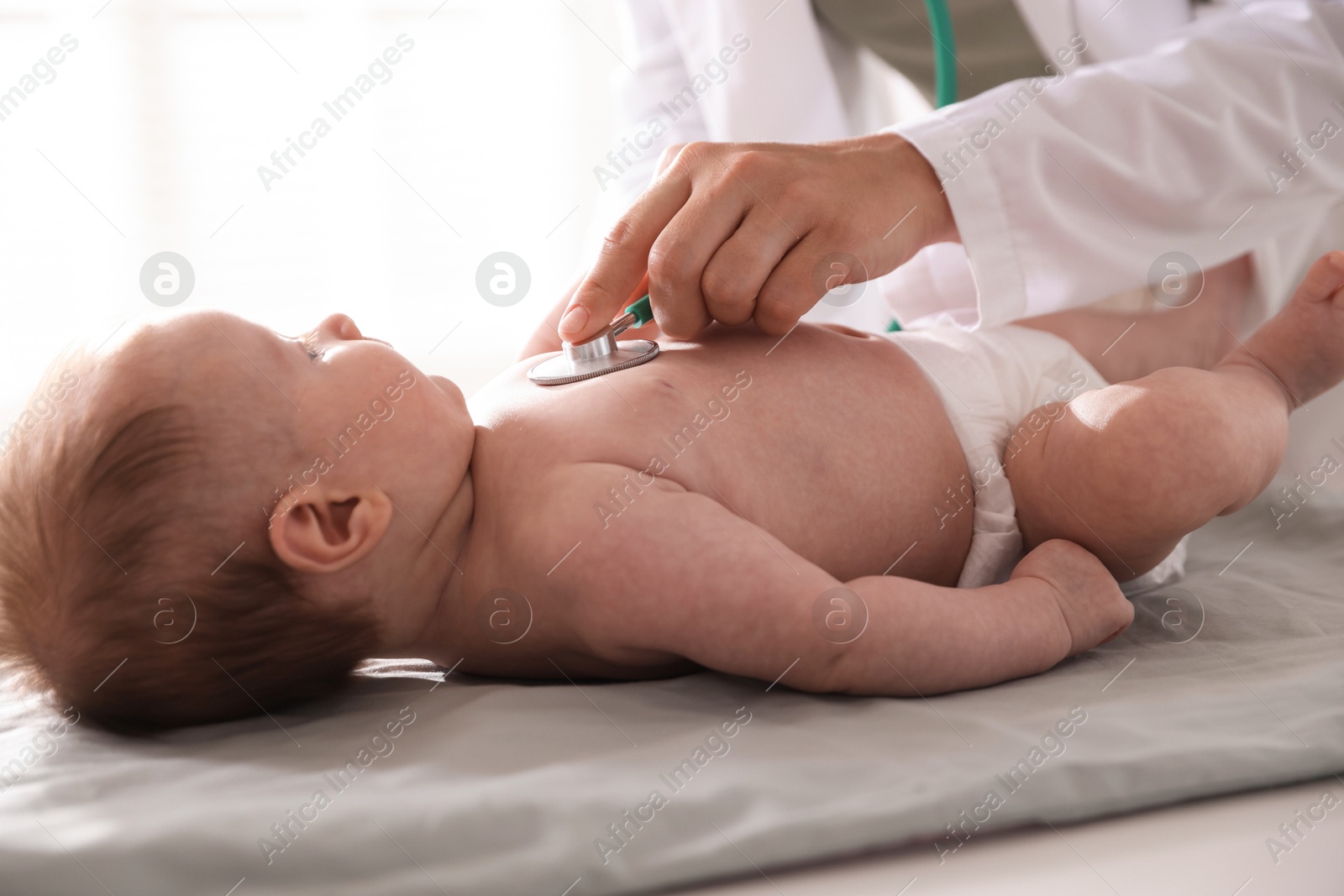 Pediatrician examining baby with stethoscope at table in clinic, closeup Photo of Pediatrician examining baby with stethoscope at table in clinic, closeup