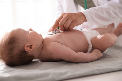 Photo of Pediatrician examining baby with stethoscope at table in clinic, closeup