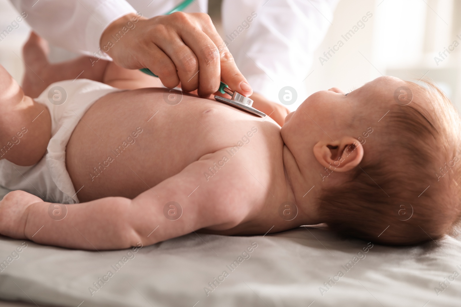 Pediatrician examining baby with stethoscope at table in clinic, closeup Photo of Pediatrician examining baby with stethoscope at table in clinic, closeup