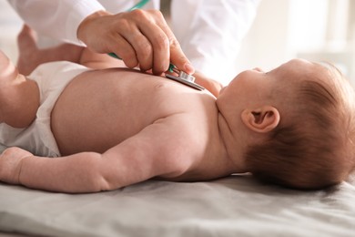 Photo of Pediatrician examining baby with stethoscope at table in clinic, closeup