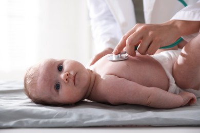 Photo of Pediatrician examining baby with stethoscope at table in clinic, closeup