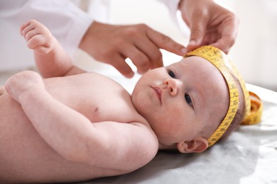 Photo of Pediatrician measuring baby's head with tape at table in clinic, closeup