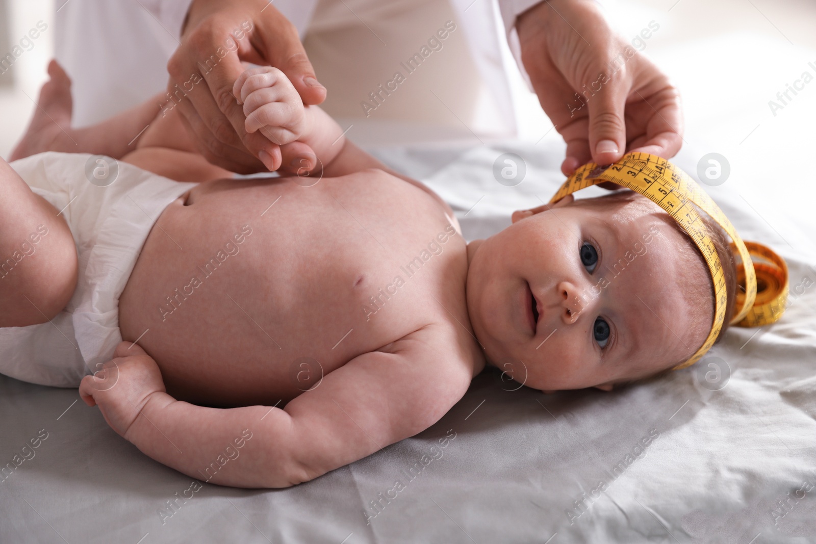 Pediatrician measuring baby's head with tape at table in clinic, closeup Photo of Pediatrician measuring baby's head with tape at table in clinic, closeup