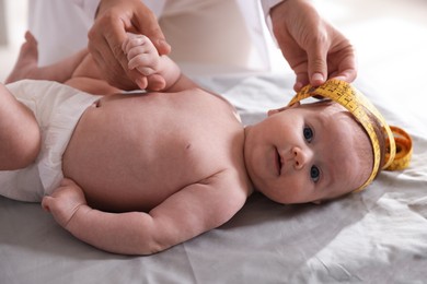 Photo of Pediatrician measuring baby's head with tape at table in clinic, closeup