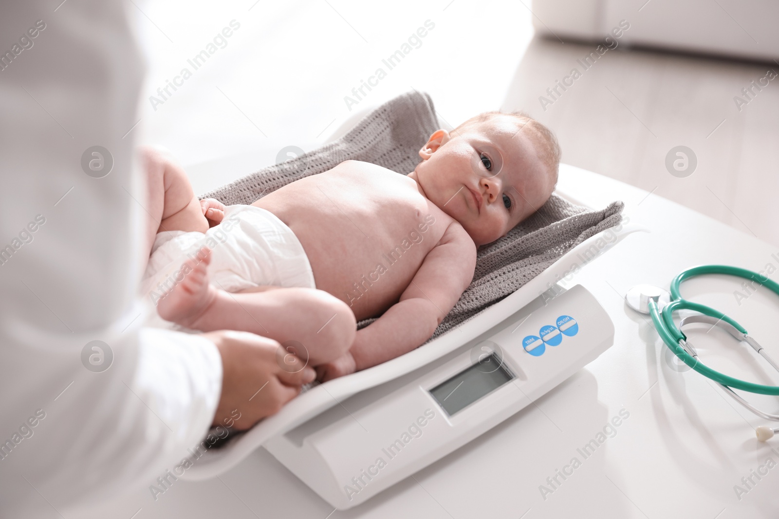 Pediatrician weighting baby with scales at white table in clinic, closeup Photo of Pediatrician weighting baby with scales at white table in clinic, closeup