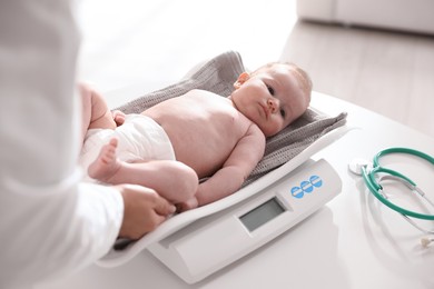 Photo of Pediatrician weighting baby with scales at white table in clinic, closeup