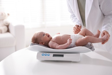 Photo of Pediatrician weighting baby with scales at white table in clinic, closeup