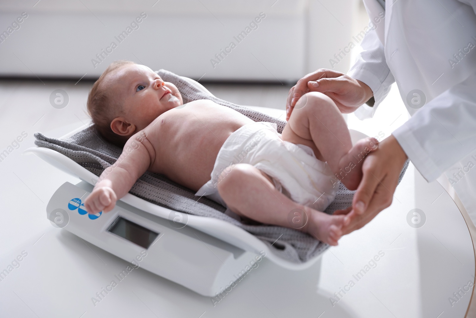 Pediatrician weighting baby with scales at white table in clinic, closeup Photo of Pediatrician weighting baby with scales at white table in clinic, closeup