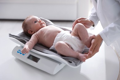 Photo of Pediatrician weighting baby with scales at white table in clinic, closeup
