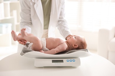 Photo of Pediatrician weighting baby with scales at white table in clinic, closeup