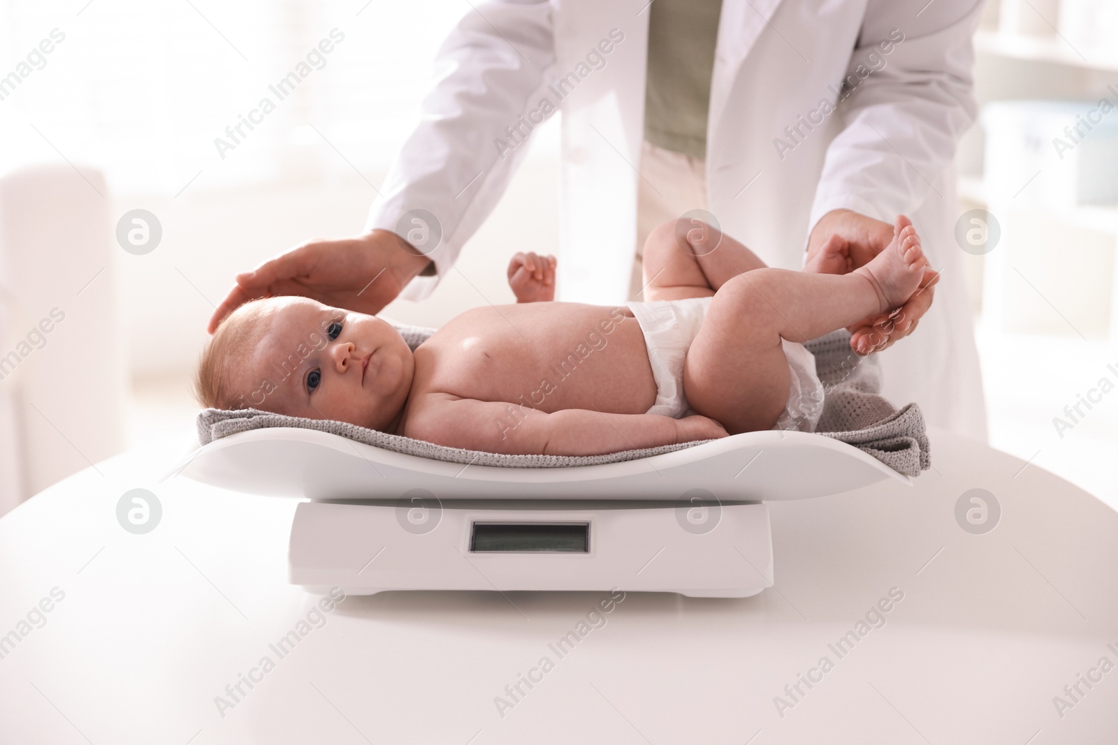 Pediatrician weighting baby with scales at white table in clinic, closeup Photo of Pediatrician weighting baby with scales at white table in clinic, closeup