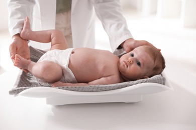 Photo of Pediatrician weighting baby with scales at white table in clinic, closeup