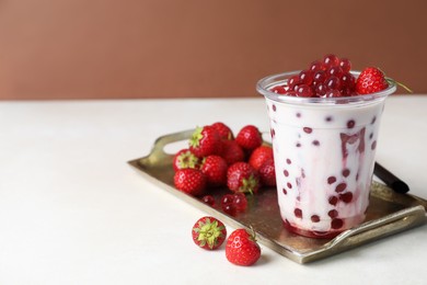 Photo of Tasty milk bubble tea in plastic cup and strawberries on white table, closeup. Space for text
