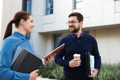 Photo of Happy coworkers with tablet discussing something near office building