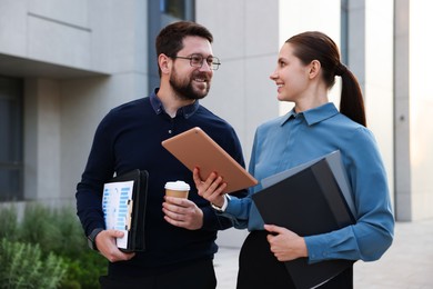 Photo of Happy coworkers with tablet discussing something near office building