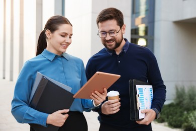 Photo of Happy coworkers with tablet discussing something near office building