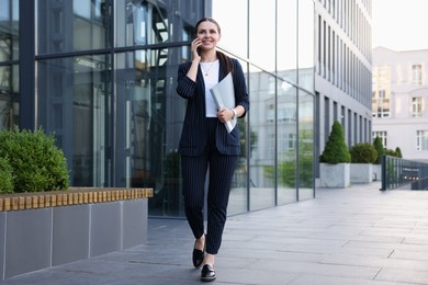 Photo of Happy businesswoman talking on phone near office building