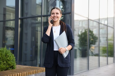 Photo of Happy businesswoman talking on phone near office building