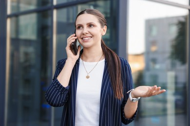 Photo of Happy businesswoman talking on phone near office building