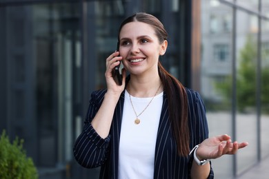 Photo of Happy businesswoman talking on phone near office building