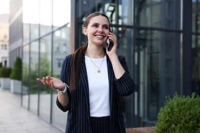 Photo of Happy businesswoman talking on phone near office building