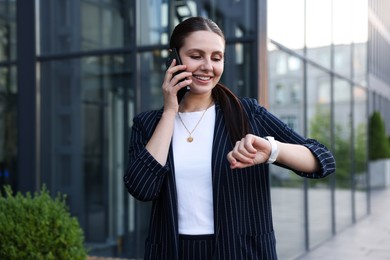 Photo of Happy businesswoman talking on phone near office building