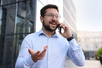 Photo of Happy businessman talking on phone near office building