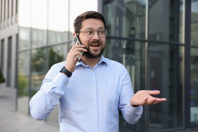 Photo of Happy businessman talking on phone near office building