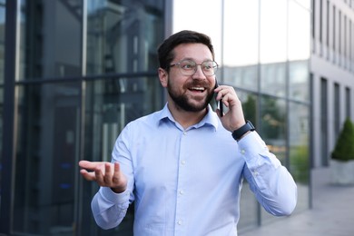 Photo of Happy businessman talking on phone near office building