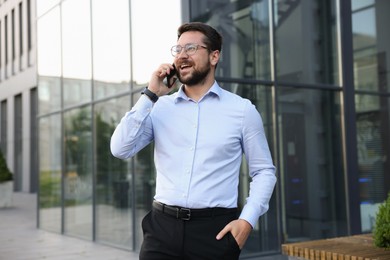 Photo of Happy businessman talking on phone near office building
