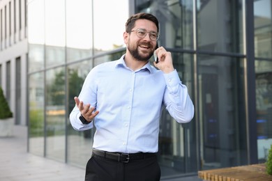 Photo of Happy businessman talking on phone near office building