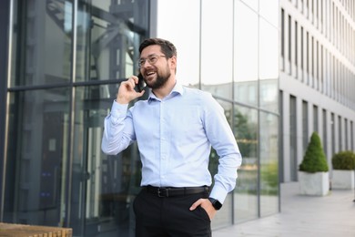 Photo of Happy businessman talking on phone near office building