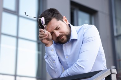 Photo of Tired businessman with glasses outside office building