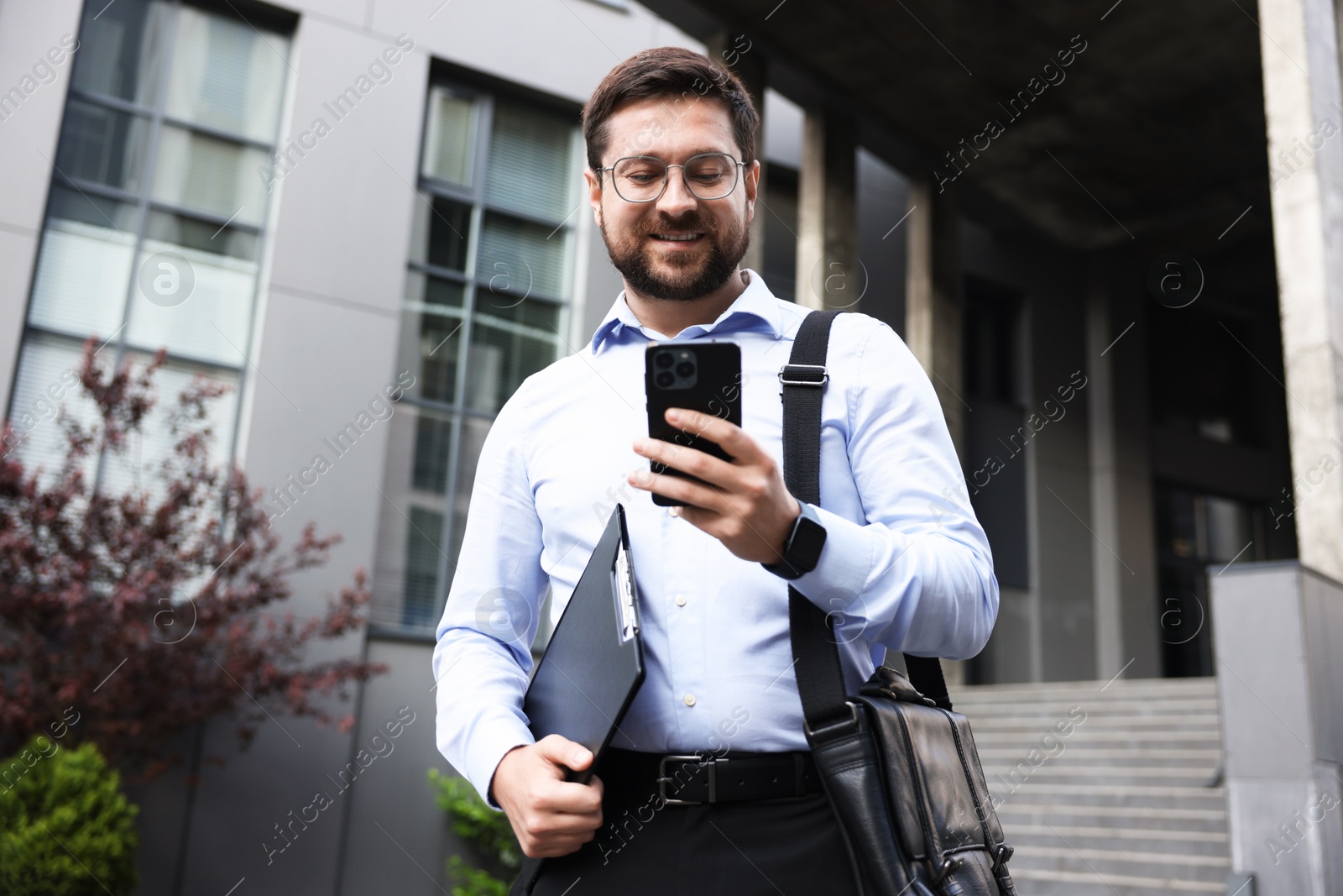 Successful businessman with smartphone near office building Photo of Successful businessman with smartphone near office building