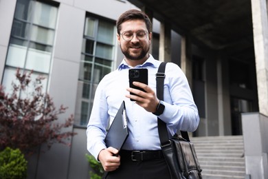 Photo of Successful businessman with smartphone near office building
