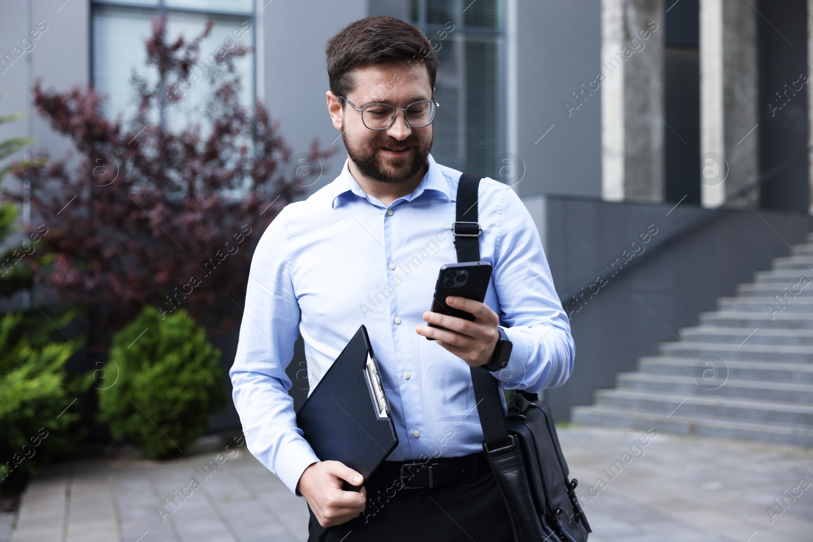 Photo of Successful businessman with smartphone near office building