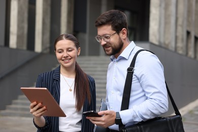 Photo of Happy coworkers with tablet and smartphone near office building