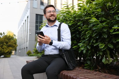 Photo of Successful businessman with smartphone on bench near office building