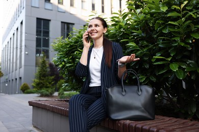 Photo of Successful businesswoman talking on phone near office building