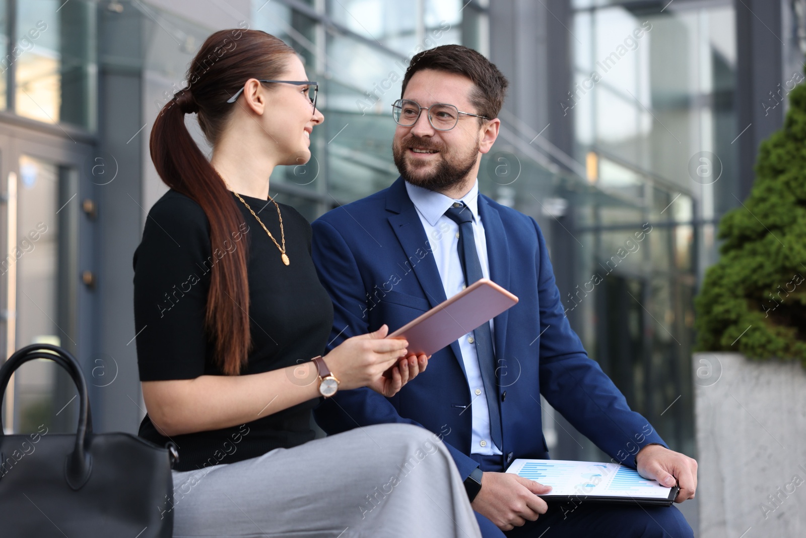 Happy coworkers with tablet discussing something near office building Photo of Happy coworkers with tablet discussing something near office building